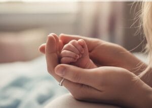 Exhausted mother holding newborn baby's hand, representing postpartum challenges and sanity-saving moments."